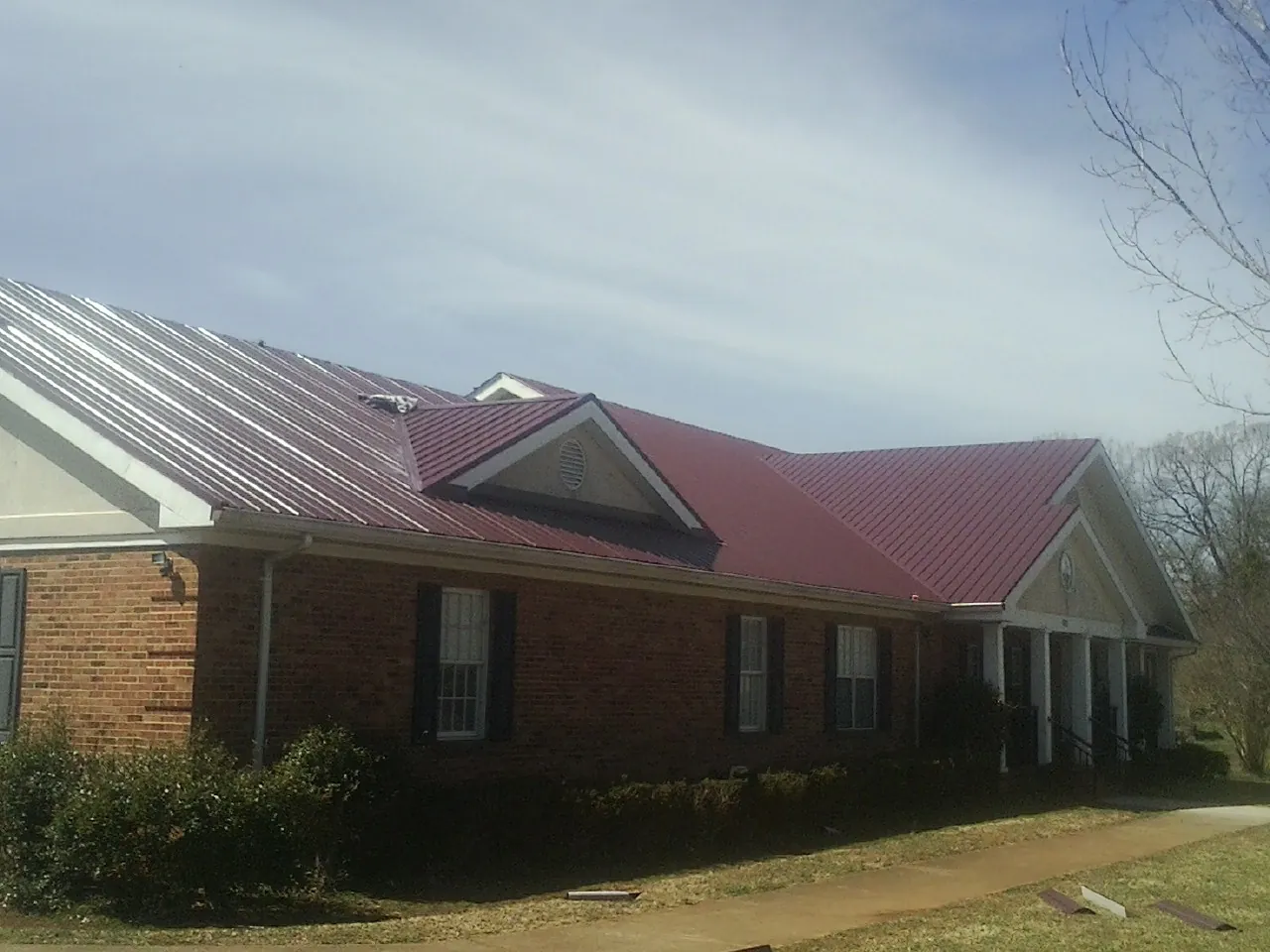 Red metal roof with gabled entries on a long brick building, from a Hail Damage Roof Repair job in Ramsey
