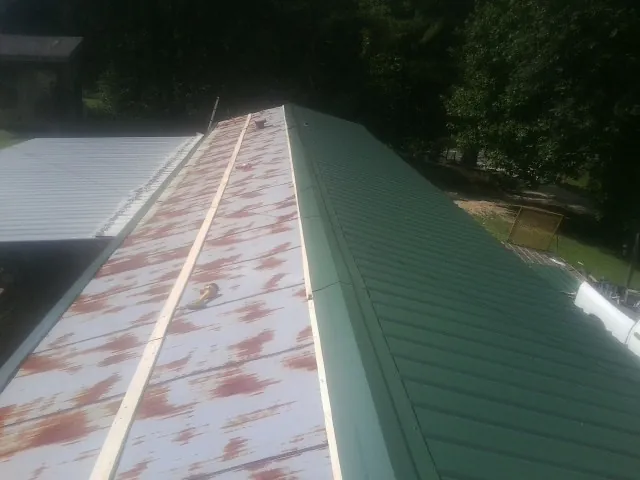 Old rusted panels beside newly installed green metal roofing — Wind Damage Roof Repair by Roofing Brothers in Ramsey