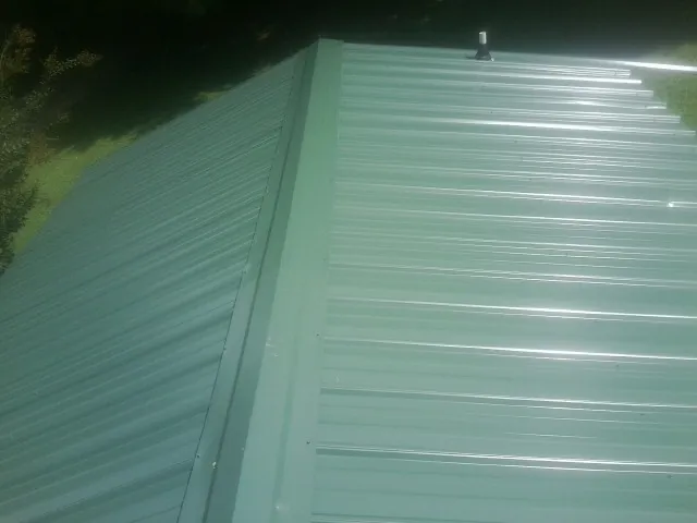 New green metal panels meeting at the ridge of a roof — Flat Roof Repair work by our crew in Ramsey