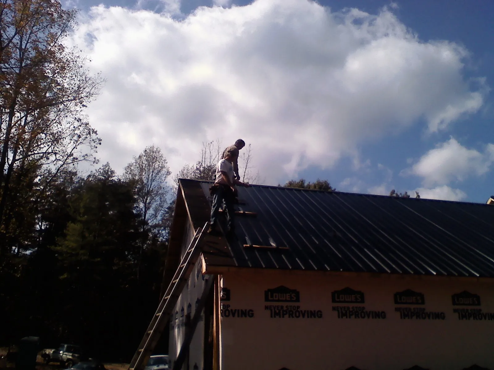 Roofer fastening dark metal panels high against a cloudy sky, from a Roof Inspection job in Ramsey