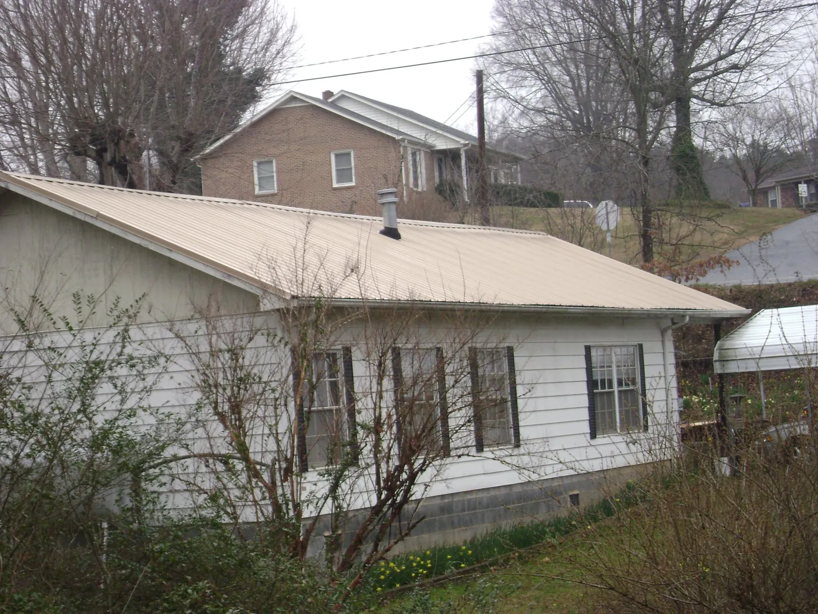 Tan metal roof on a white sided house set into a hillside — Commercial Roofing by Roofing Brothers in Ramsey
